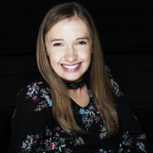 Kyann, a white woman with long, blonde hair smiles at the camera. She is wearing a dark floral top.